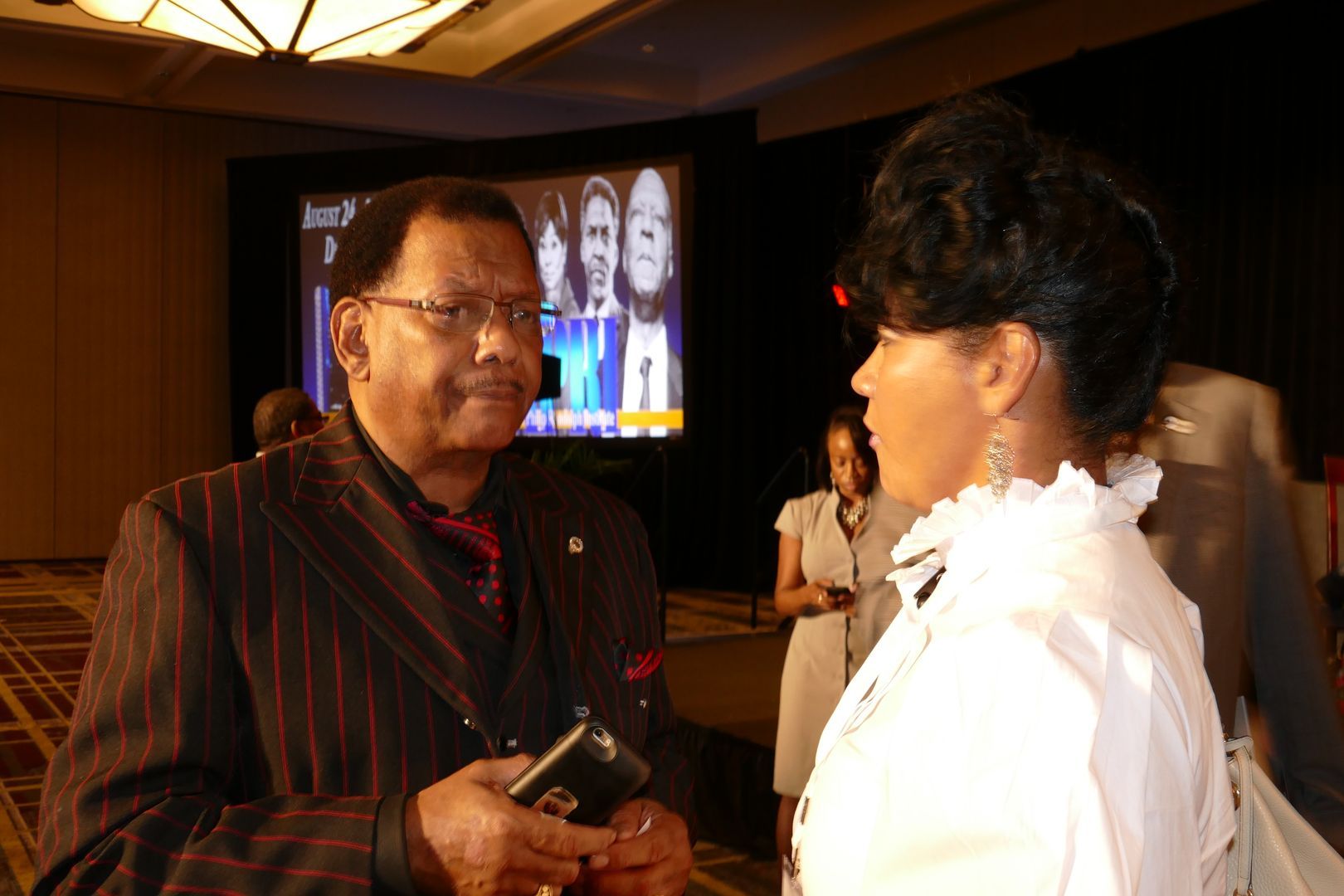 A man in a suit and tie is talking to a woman in a white shirt  at an APRI event