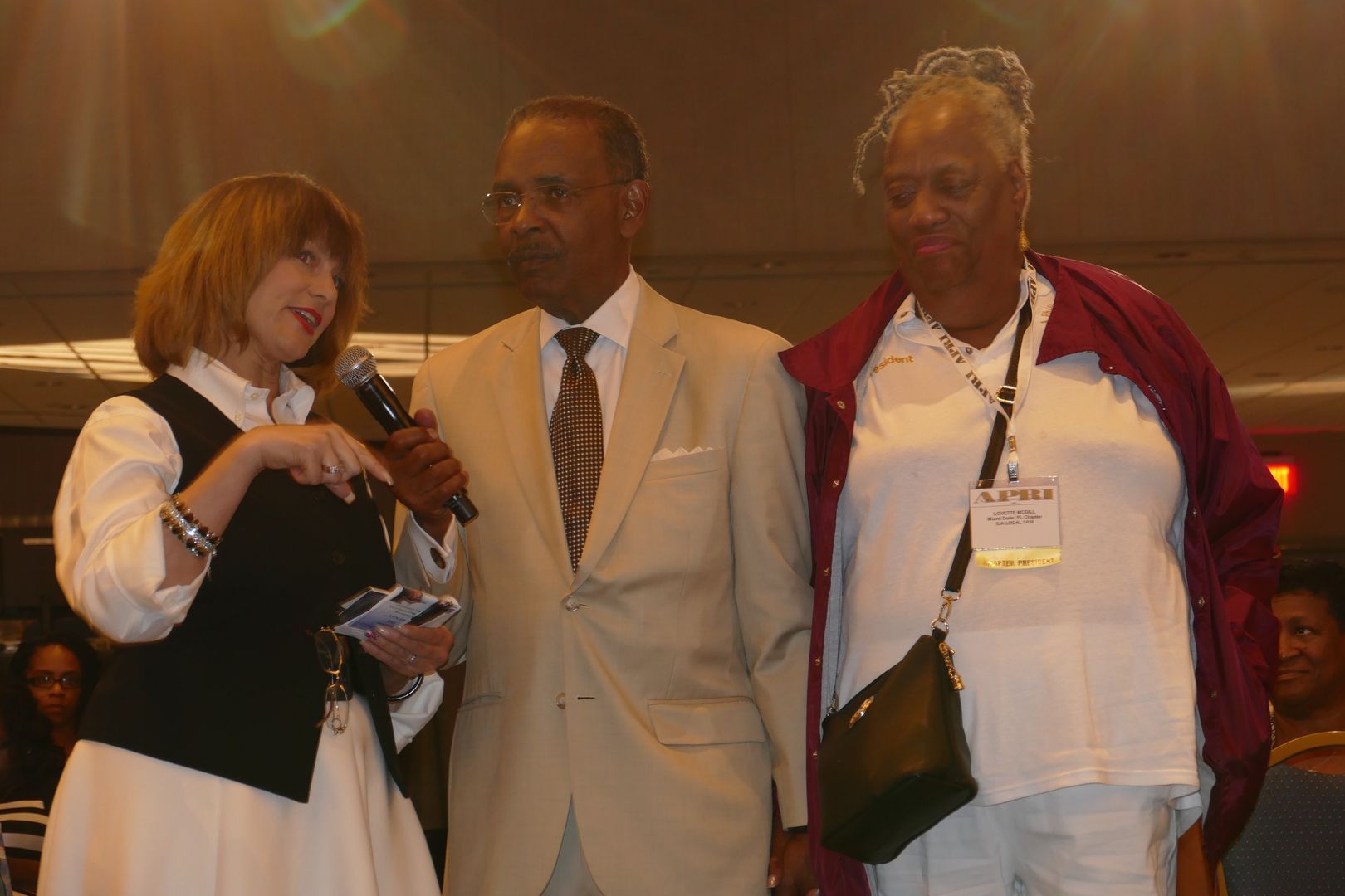 A man in a suit and tie is standing next to a woman holding a microphone  at an APRI event
