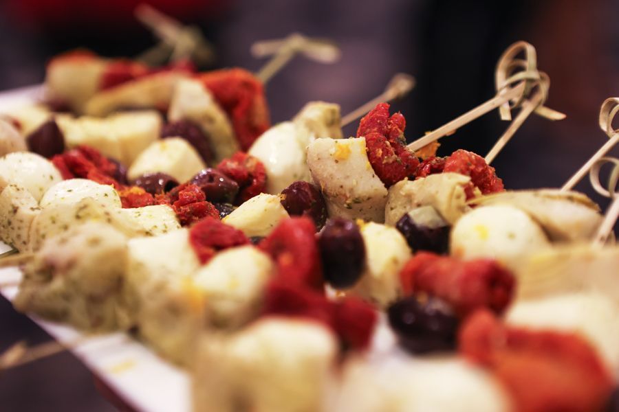 Skewers with red tomatoes, olives, cheese, and herbs on a white platter.