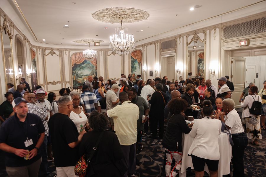Large gathering in a decorated ballroom. Mostly Black people are socializing, drinking, and networking.