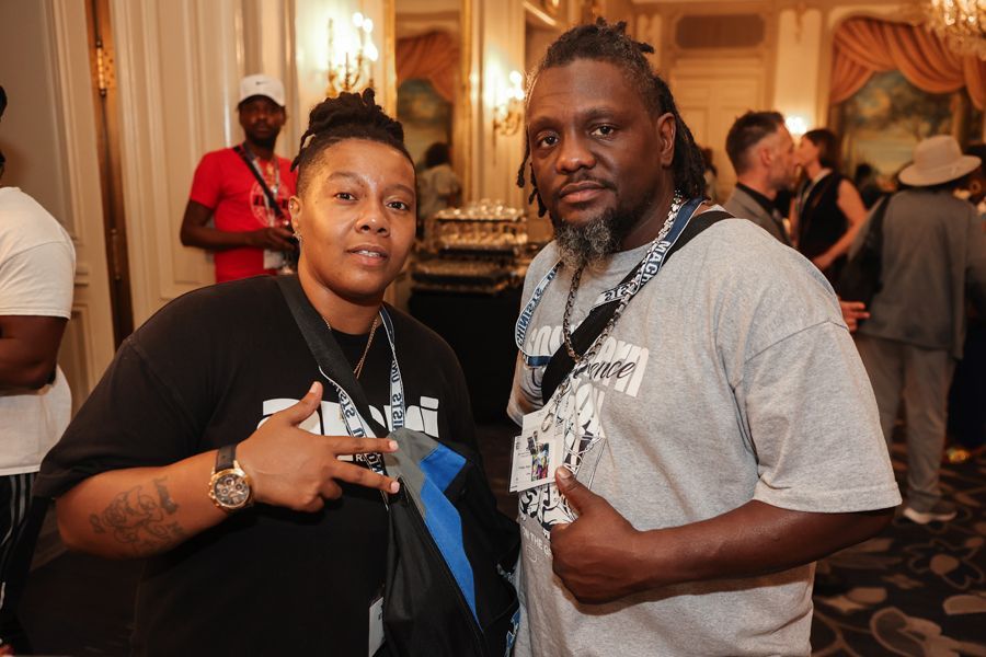 Two people with lanyards pose for a photo in a room with a chandelier.