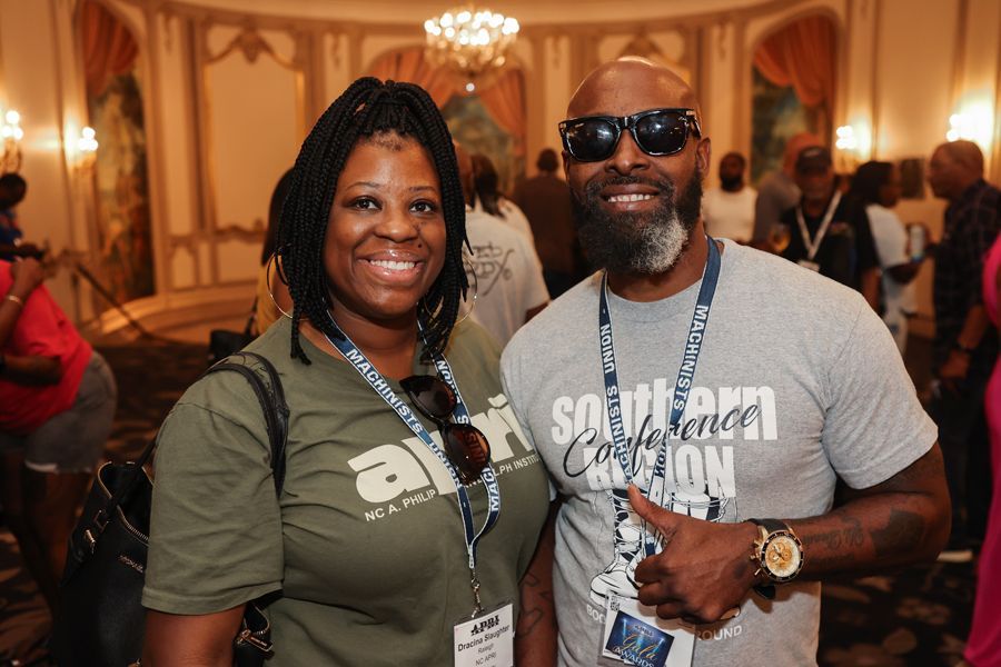 Two people smiling. Woman with dreadlocks, olive shirt, man with sunglasses, gray shirt, and thumb up.