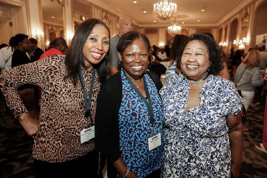 Three smiling Black women pose for a photo at an event, in a well-lit room.