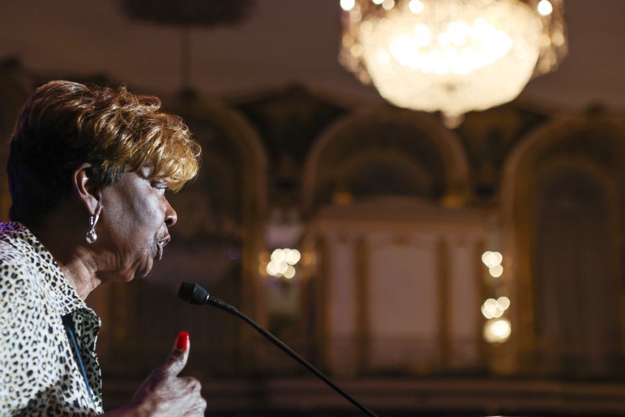 President Brown of APRI speaking at a podium, looking left, wearing a leopard print top, with a chandelier in the background.