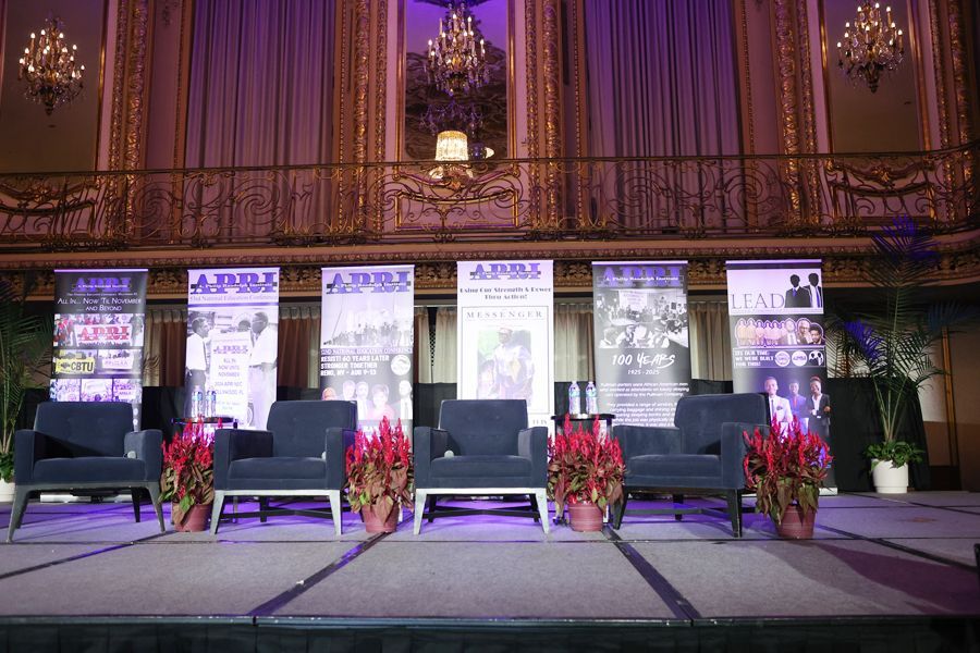 Panel stage with chairs, banners, and floral arrangements. Formal setting with balcony and ornate decor.