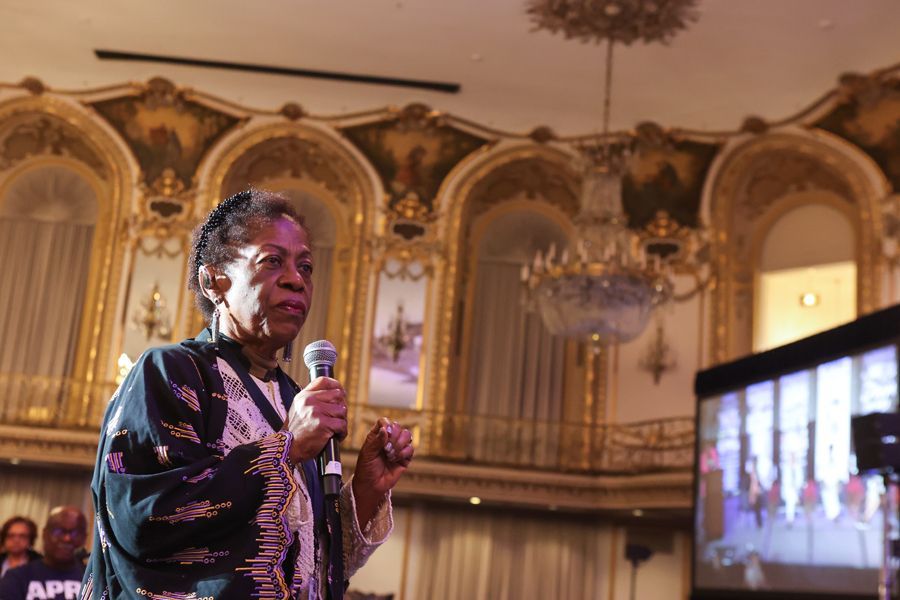 Woman engaged at an conference, holding a microphone, in a grand hall with ornate decor.