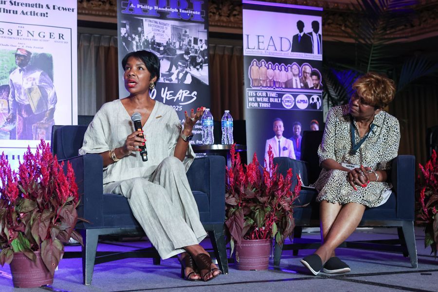 Two women seated on stage, one speaking into a microphone.