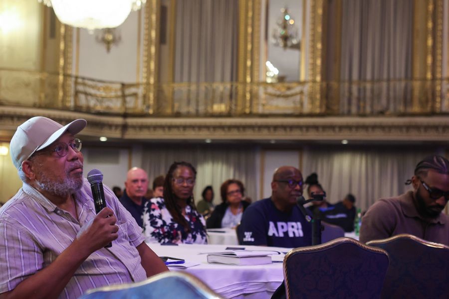 Man with microphone asking a question at a conference in an ornate ballroom.