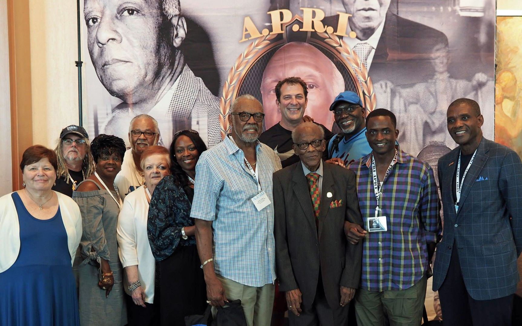 A group of people are posing for a picture in front of a picture of a man.