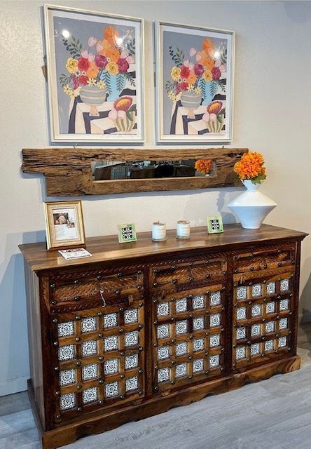 A wooden dresser with two paintings on the wall above it