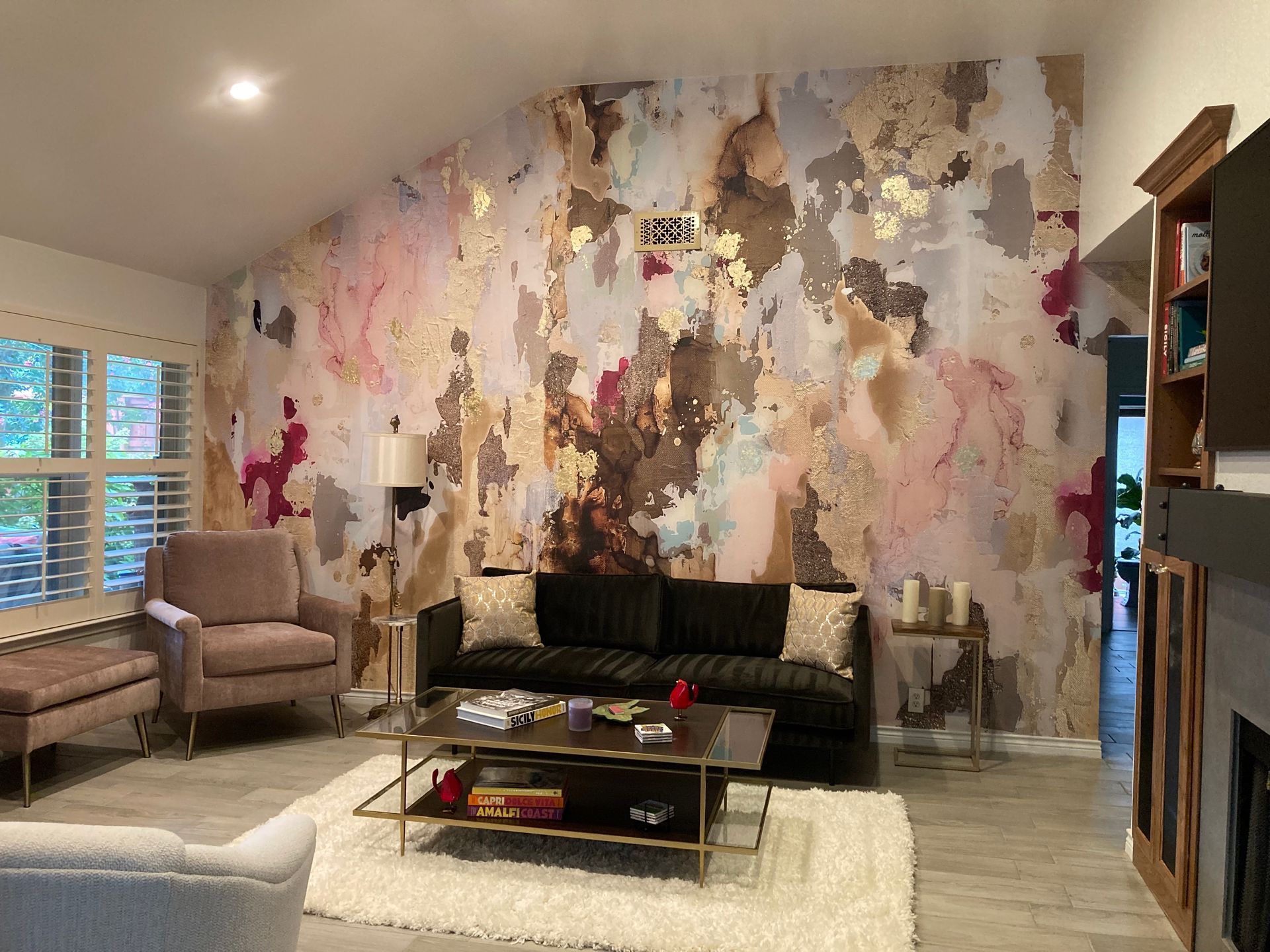 A living room with a couch , chair , coffee table and a large wall mural.