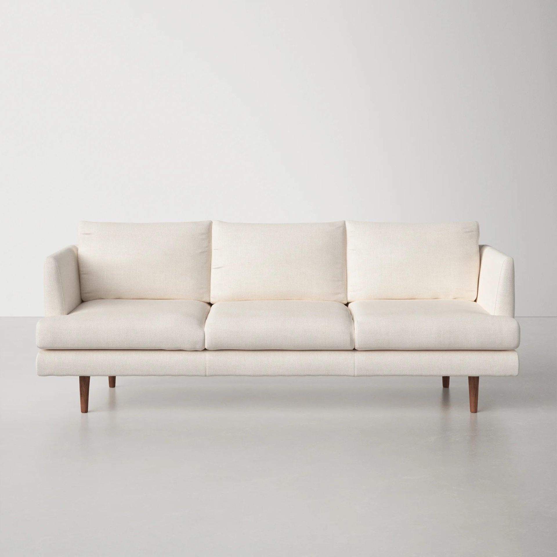 A white couch is sitting on a white floor in front of a white wall.