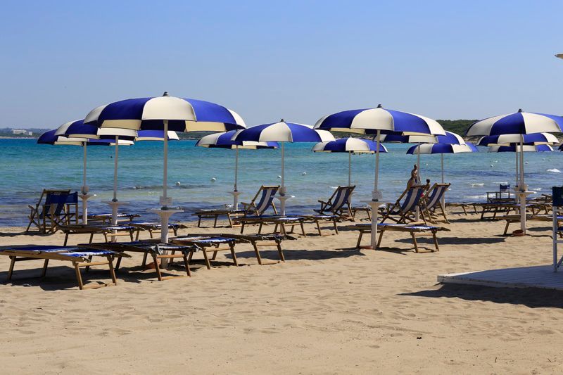 Sedie a sdraio e ombrelloni blu e bianchi su una spiaggia sabbiosa in riva al mare.
