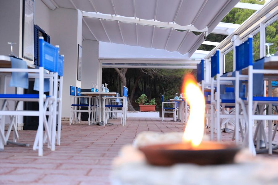 Caffè all'aperto con sedie e tavoli blu sotto una tettoia bianca, con una piccola fiamma in primo piano.