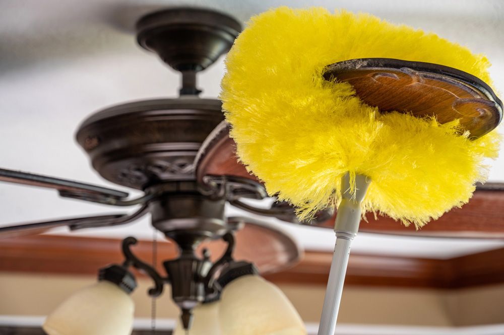 Yellow duster cleaning a brown ceiling fan with light fixtures.
