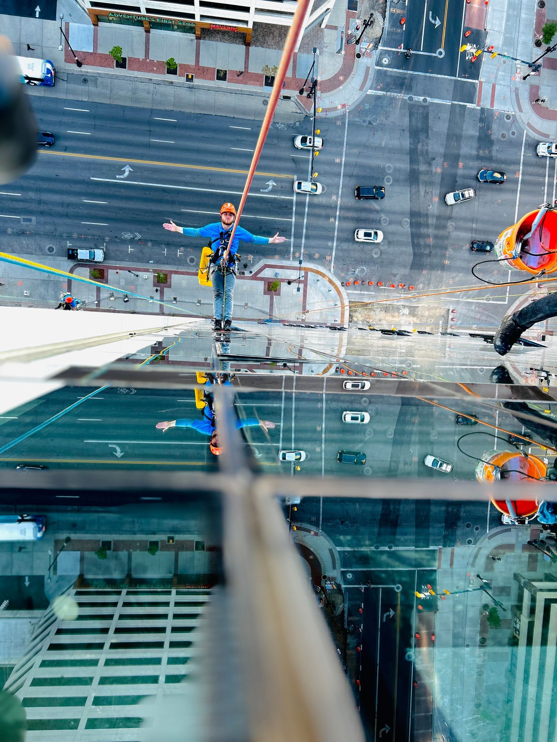 Man on ladder washing a large window with squeegee; sunny outdoors, stone wall.