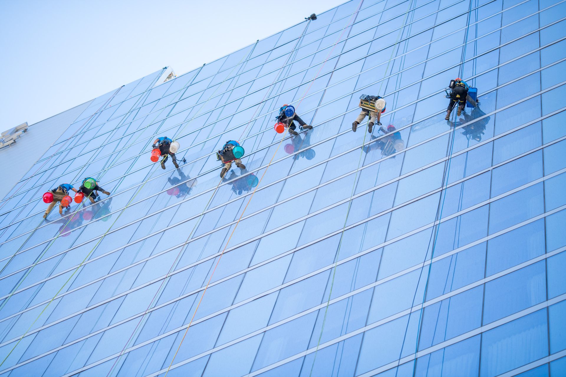 Window washer on a suspended platform cleaning a large, blue glass building.