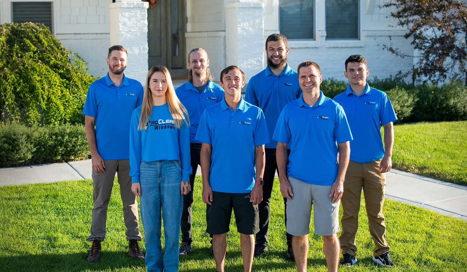 Group of people in blue shirts posing outside a building on a sunny day.