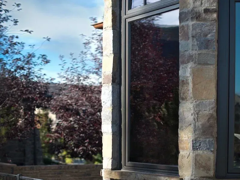 Stone wall framing a window reflecting trees with red leaves and a blue sky.