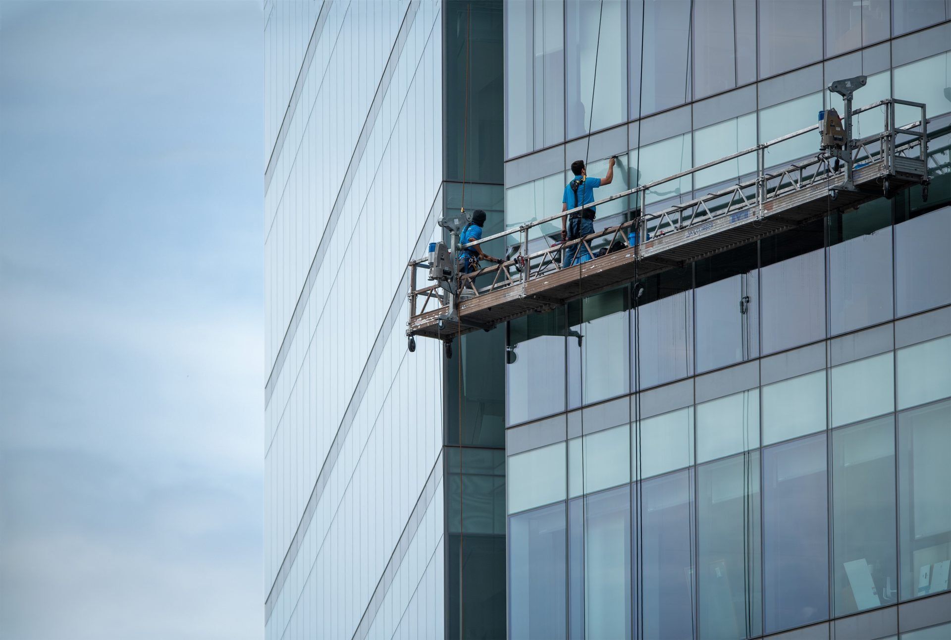 Window washers on a suspended platform cleaning a glass skyscraper facade.