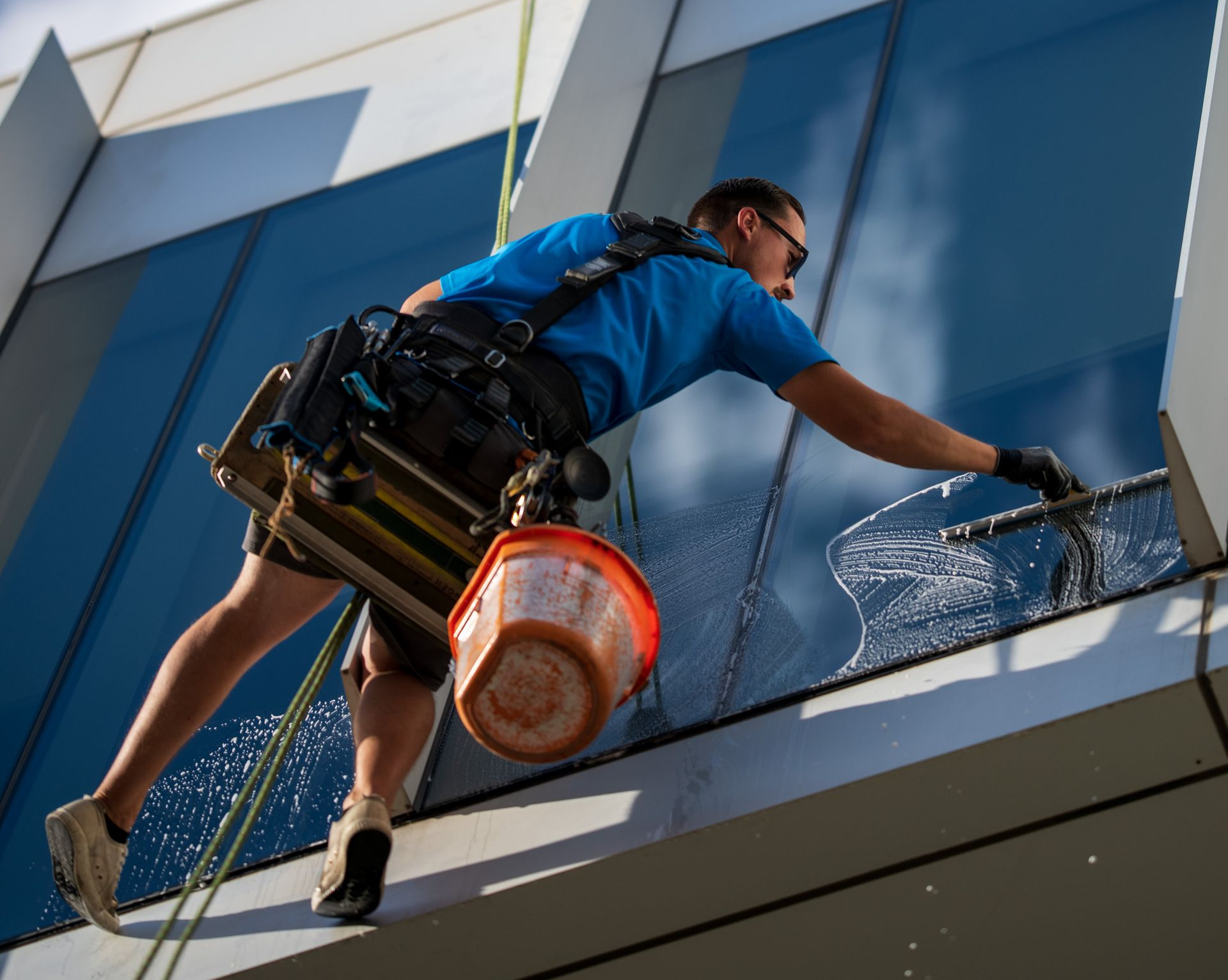 Person wearing yellow glove, using a squeegee to clean a soapy window.