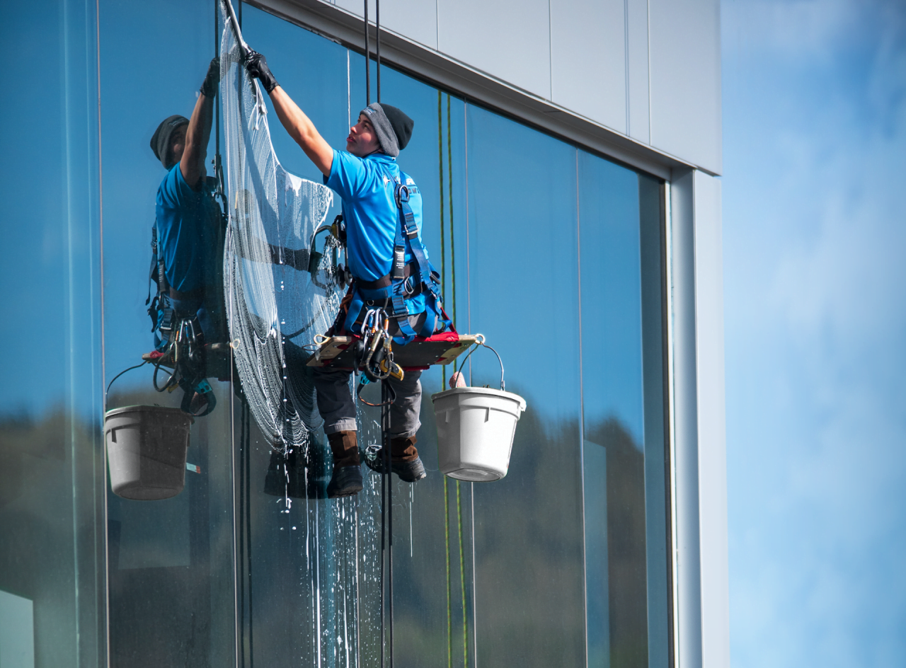 Window washer suspended from cables cleaning a tall building's glass facade.