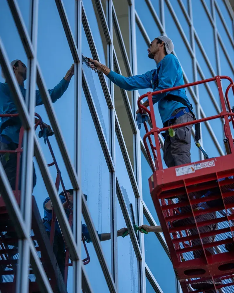 Window washer cleaning a skyscraper window from a red lift.