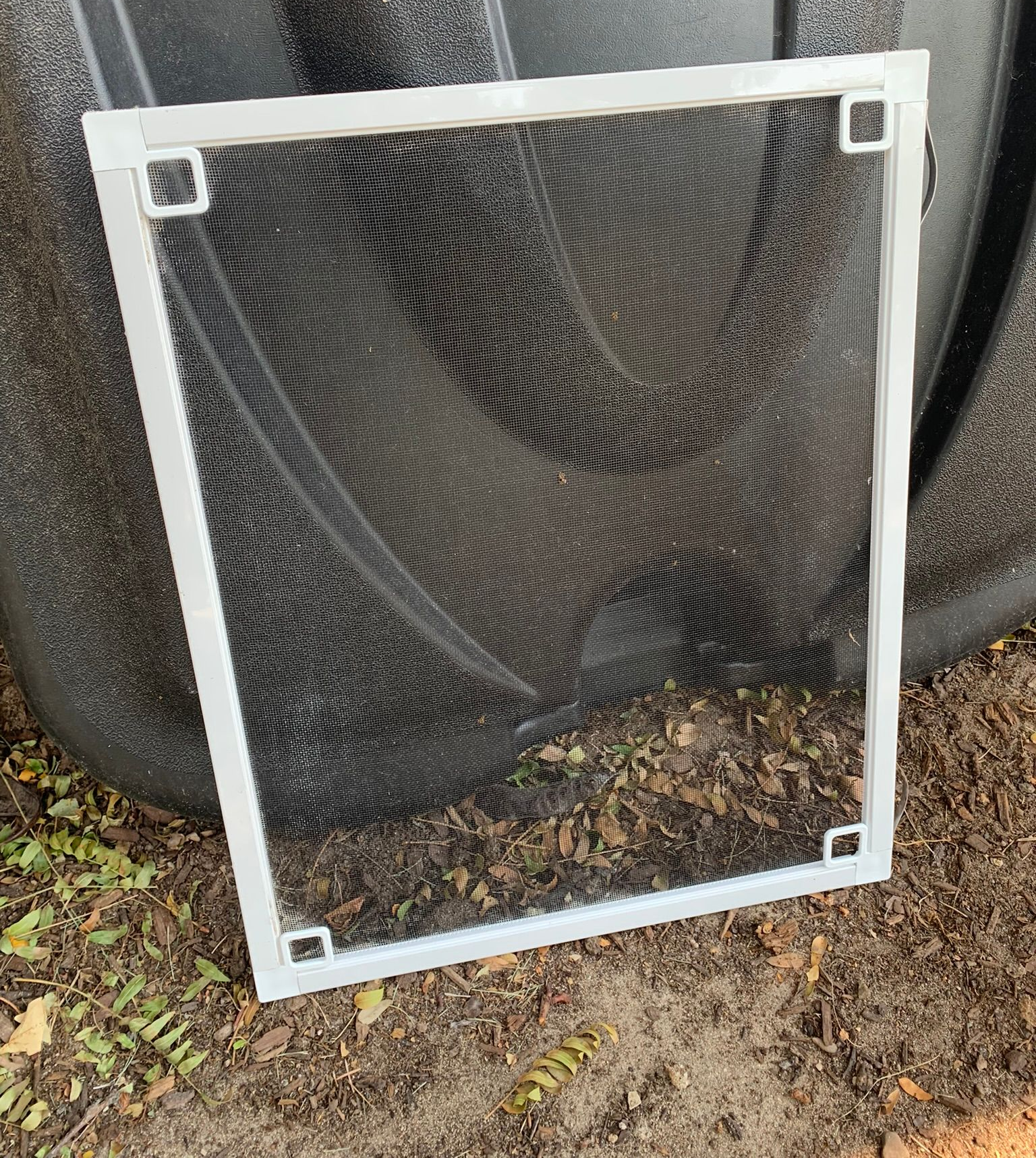 Square metal frame with black mesh screen sits on a dark, textured surface, possibly a tank.