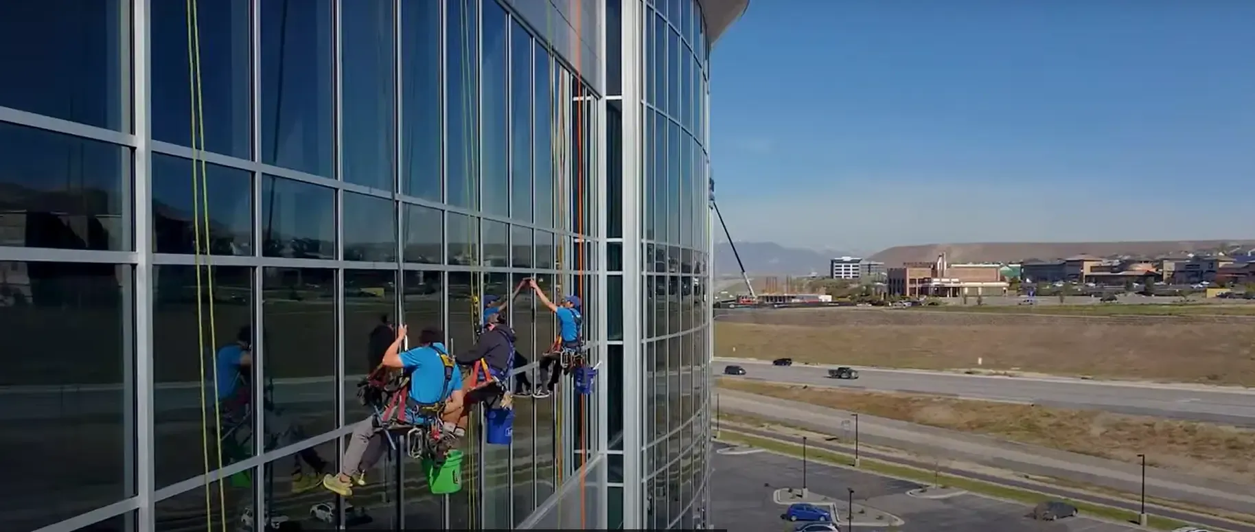 Window washers rappelling down a tall building on a sunny day.