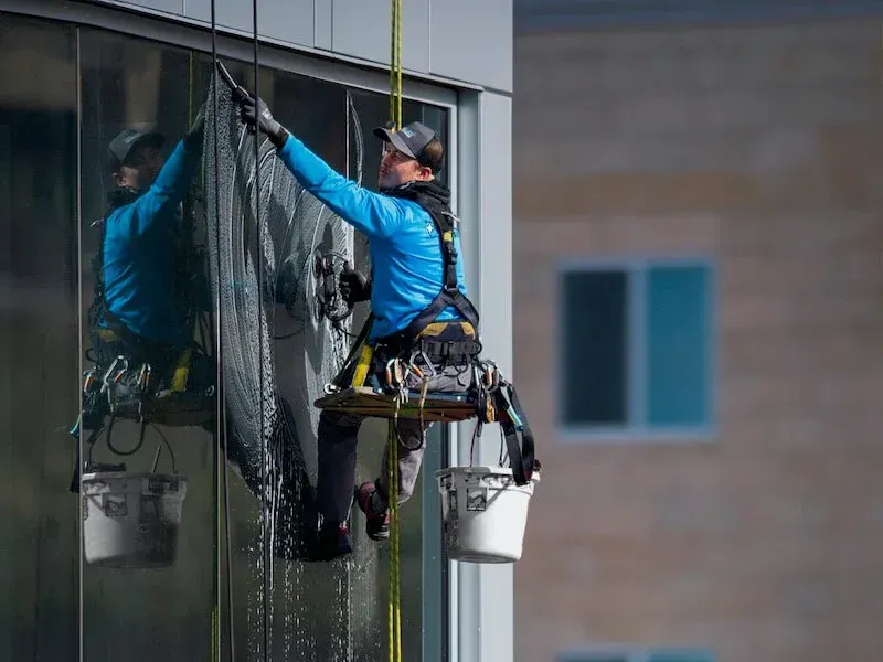 Window washer suspended on ropes cleaning a glass building.