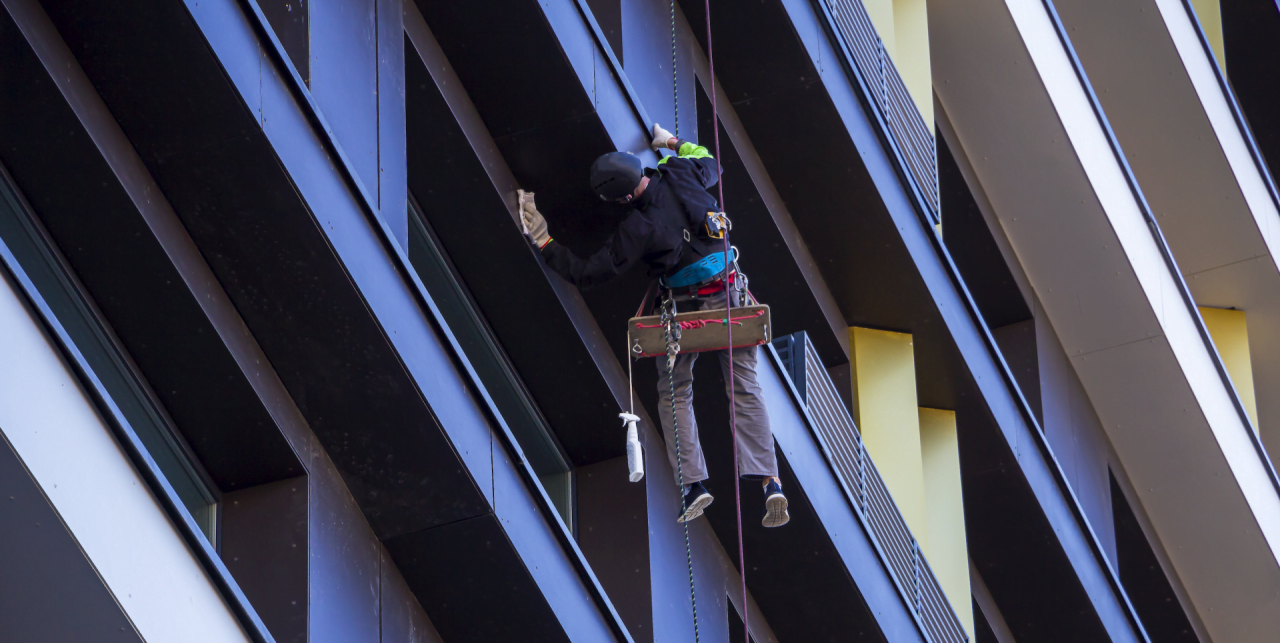 Window cleaner suspended on ropes, cleaning a building's exterior.
