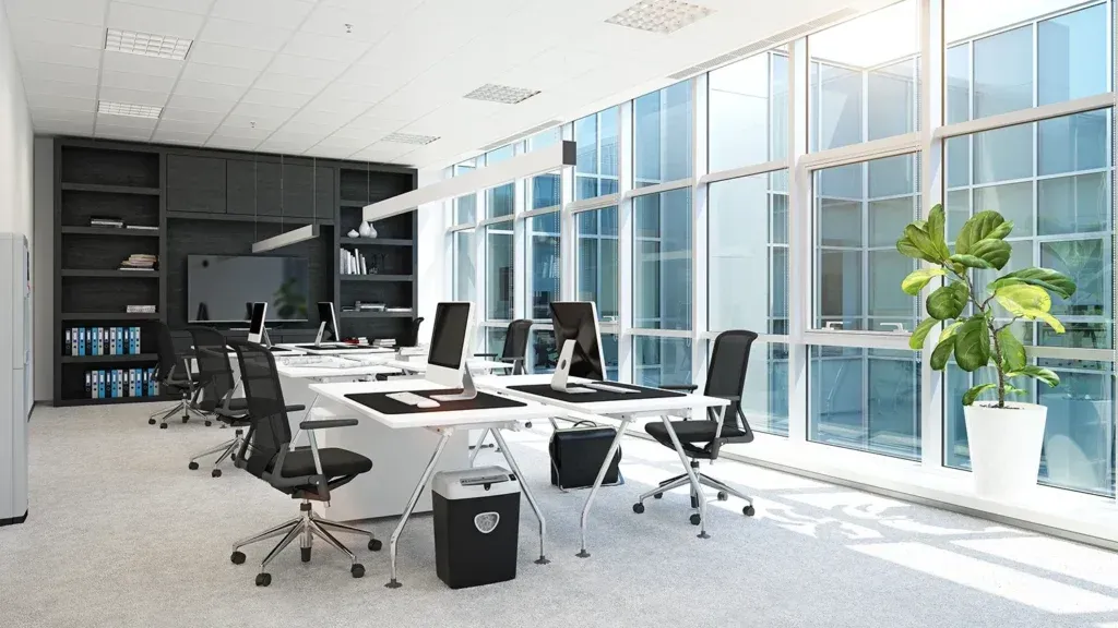Modern office with long desk, black chairs, large windows, and built-in shelving. Bright, natural light.