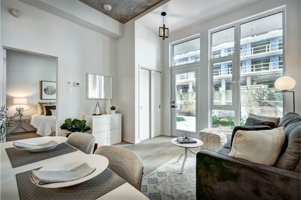 Bright, modern condo interior with dining area, living room, and large windows overlooking another building.