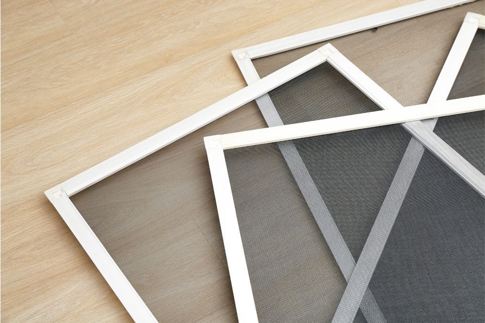 Three white-framed window screens, each with gray mesh, on a light wood surface.