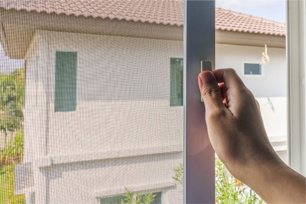 Hand opening a screen door with a house visible in the background through the screen.