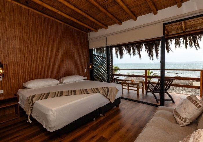 Dormitorio con vista al mar: cama King, balcón con asientos, paneles de madera, luz natural.
