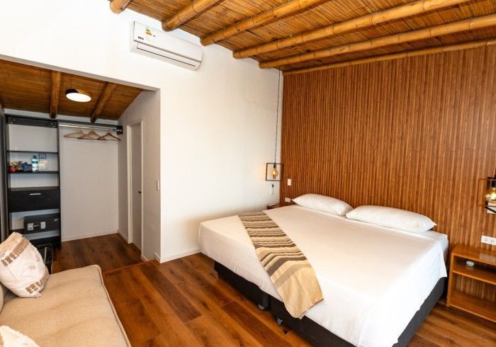 Dormitorio con techo y pared de bambú, cama, sofá pequeño y armario.