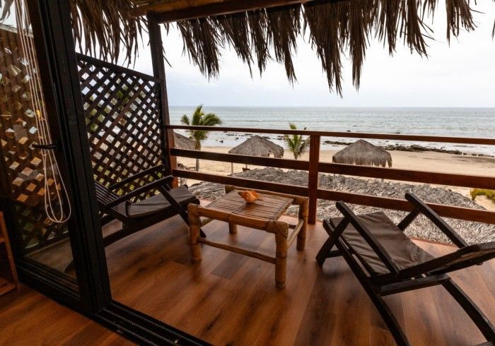 Balcón con vista al mar y techo de paja. Muebles de bambú, como sillas y mesa.