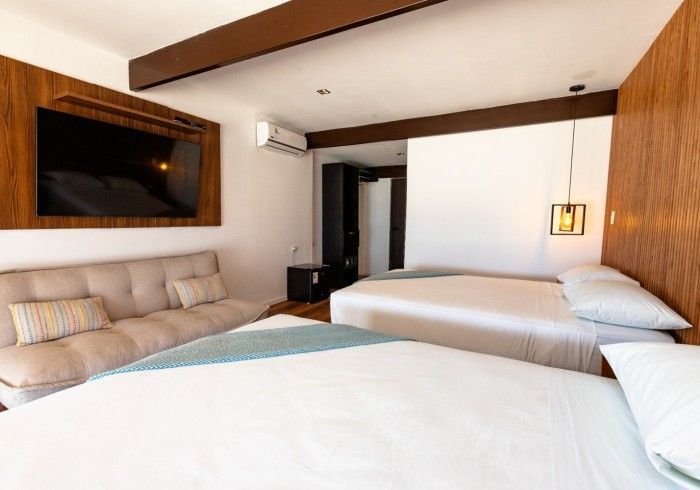 Habitación de hotel con dos camas, sofá y televisor de pared. Revestimiento de madera cálido y un interior moderno y luminoso.