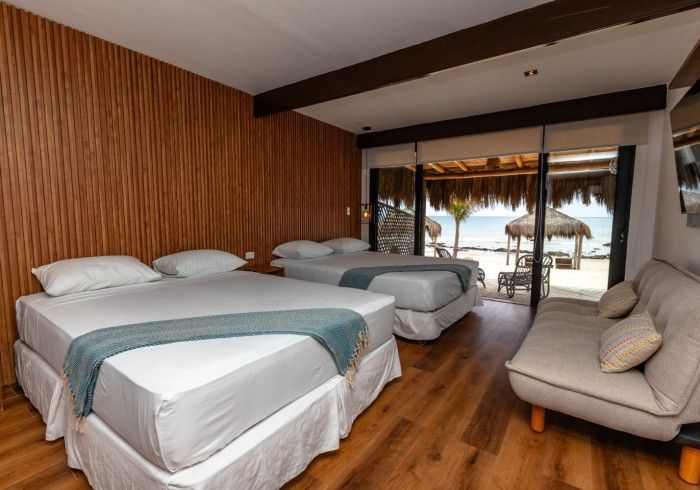 Habitación de hotel con dos camas dobles, una cama individual y un pequeño sofá. Vista al mar desde el balcón.