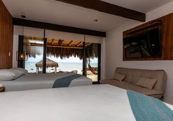 Habitación de hotel con dos camas, vista al mar y un pequeño sofá debajo de un televisor montado.