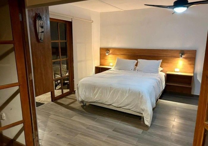 Dormitorio con cama de matrimonio, mesitas de noche y cabecero de madera; puerta abierta.