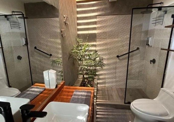 Dos cabinas de ducha con pasamanos, inodoros y bancos de madera en un entorno tipo spa.