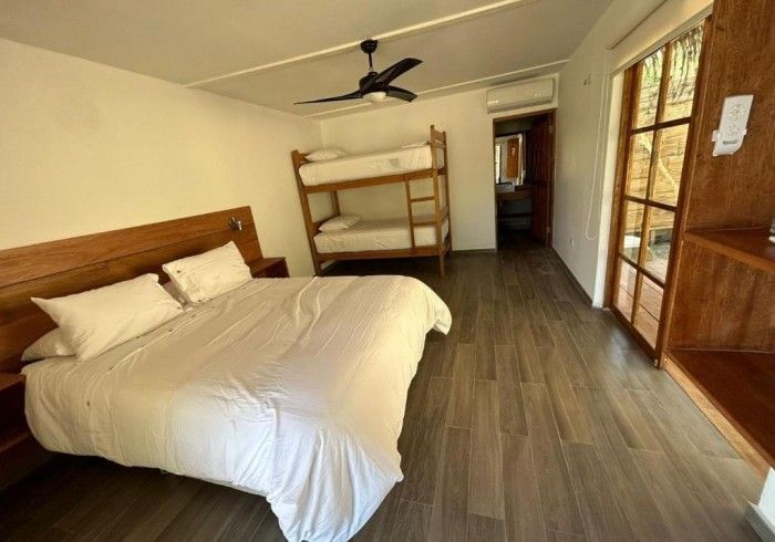 Dormitorio con cama de matrimonio y literas, suelo de madera y puerta al exterior.