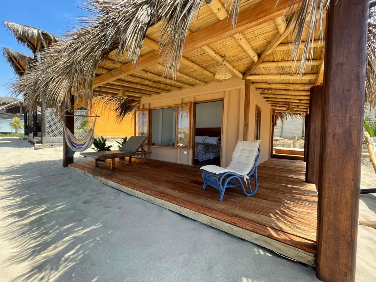 Dormitorio con cama, pequeño sofá, armario de madera, paredes blancas y techo de paja.