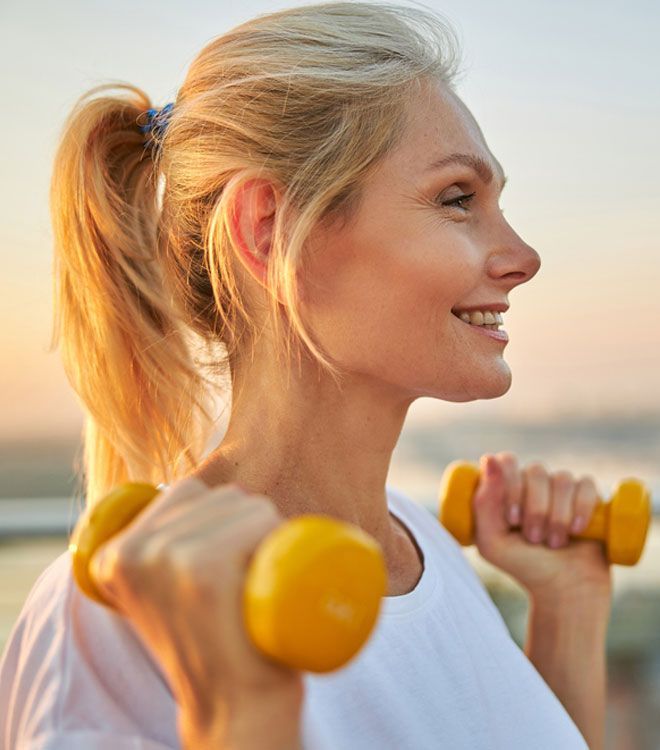 A woman is holding two yellow dumbbells in her hands.