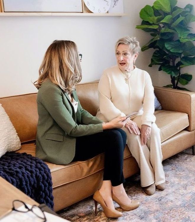 Two women are sitting on a couch talking to each other