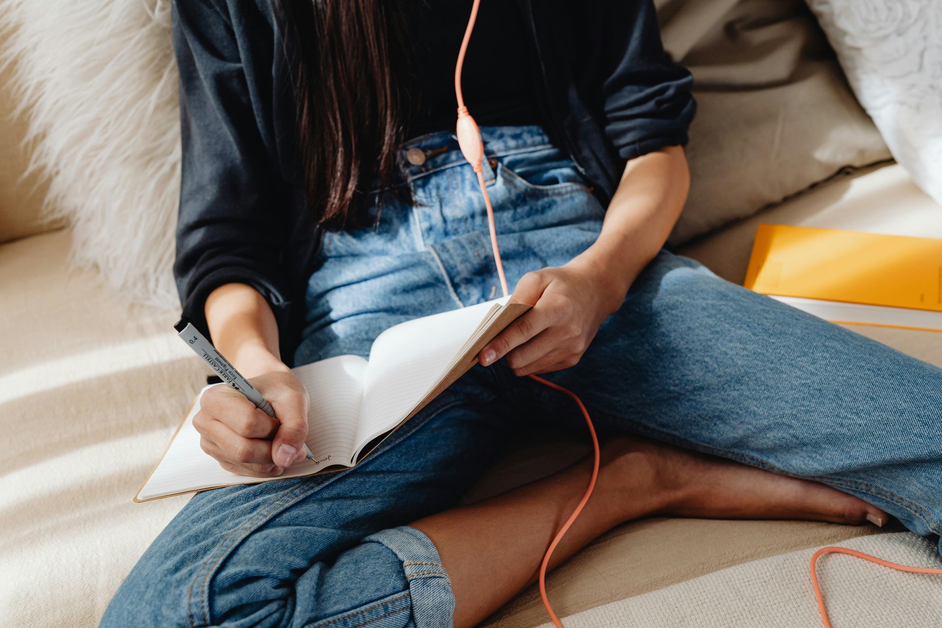 A woman is sitting on a couch writing in a notebook.