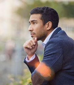 A man in a suit is sitting down with his hand on his chin.