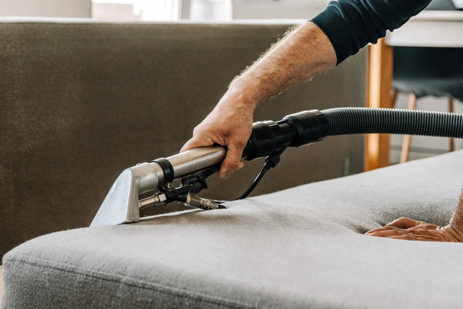 Person cleans gray couch cushion with upholstery cleaner.